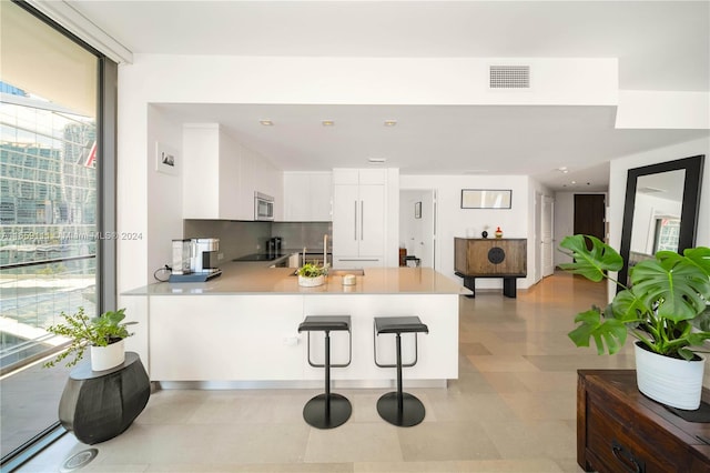 kitchen featuring tasteful backsplash, sink, white cabinetry, kitchen peninsula, and a kitchen breakfast bar