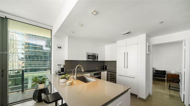 kitchen with sink, wood-type flooring, beverage cooler, white cabinetry, and a kitchen bar