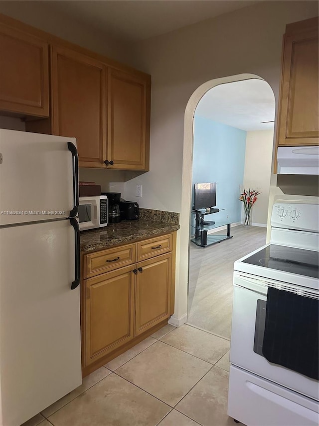 kitchen with ventilation hood, white appliances, light tile patterned flooring, and dark stone countertops