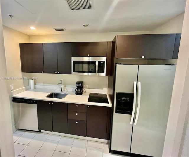 kitchen with dark brown cabinetry, light tile patterned floors, stainless steel appliances, and sink