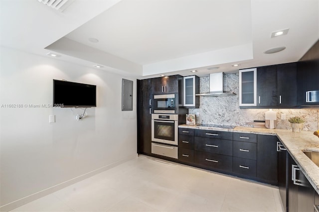 kitchen featuring a raised ceiling, wall chimney exhaust hood, light stone counters, and black appliances