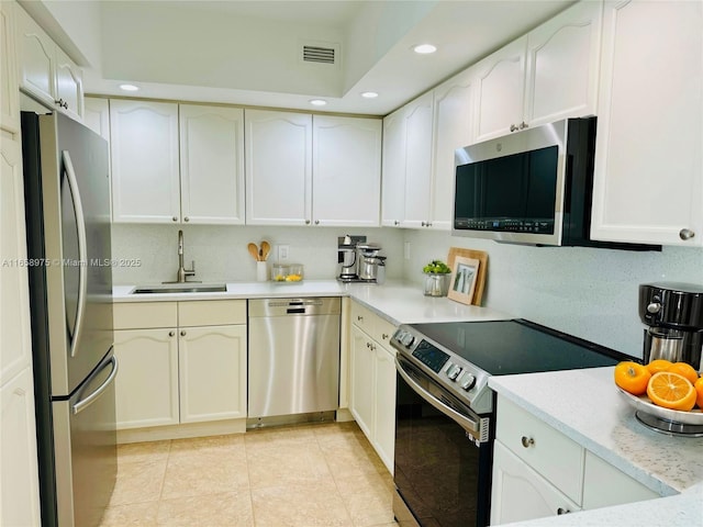 kitchen with light tile patterned flooring, sink, tasteful backsplash, stainless steel appliances, and white cabinets