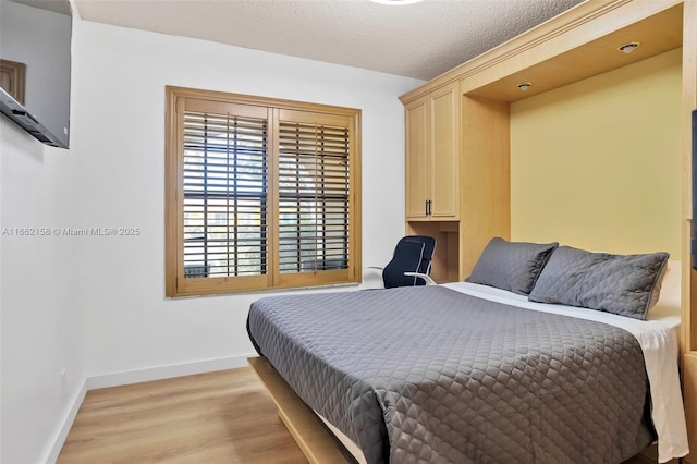 bedroom featuring a textured ceiling, built in desk, and light hardwood / wood-style flooring