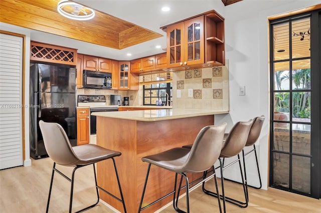 kitchen with backsplash, black appliances, sink, light wood-type flooring, and kitchen peninsula