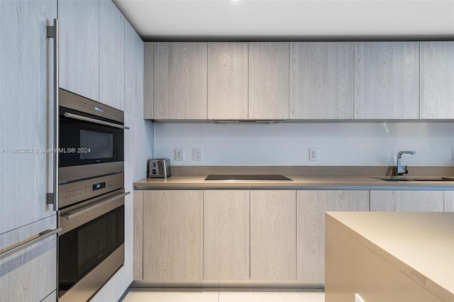 kitchen with a sink, black electric stovetop, modern cabinets, and light countertops