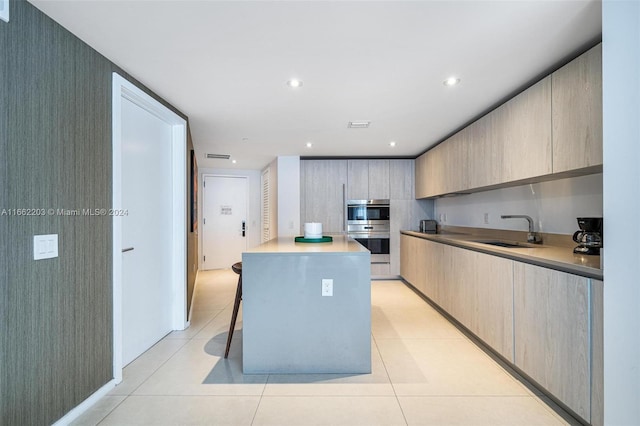 kitchen featuring light brown cabinets, light tile patterned floors, sink, a kitchen island, and double oven