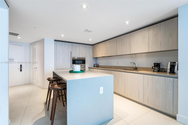 kitchen with visible vents, a kitchen island, a breakfast bar, light tile patterned floors, and a sink