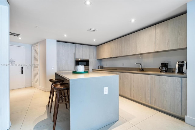 kitchen with light tile patterned floors, light brown cabinets, sink, and oven