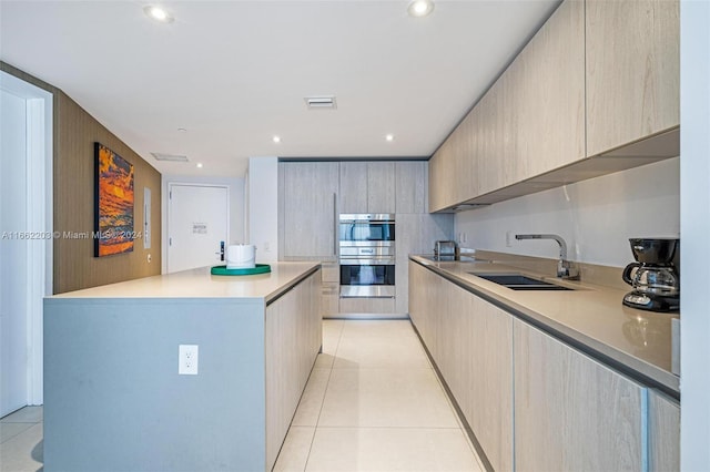 kitchen with a center island, sink, light brown cabinets, light tile patterned floors, and double oven