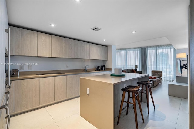 kitchen featuring black electric stovetop, sink, a kitchen bar, a kitchen island, and light brown cabinets