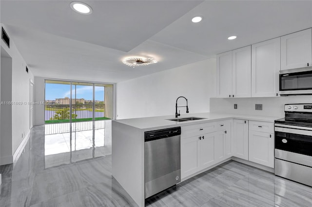 kitchen with sink, appliances with stainless steel finishes, kitchen peninsula, and white cabinetry