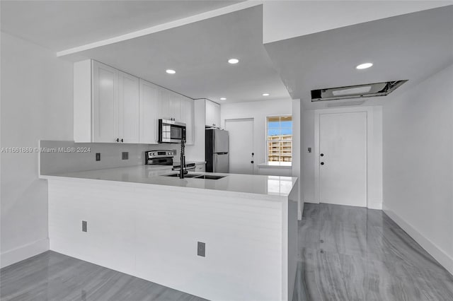 kitchen with white cabinets, light hardwood / wood-style floors, kitchen peninsula, and appliances with stainless steel finishes