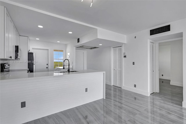 kitchen featuring range, stainless steel fridge, white cabinets, kitchen peninsula, and sink