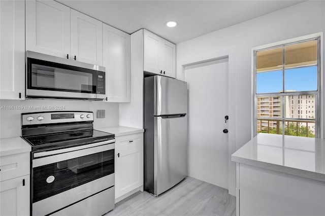 kitchen with white cabinetry, light hardwood / wood-style floors, appliances with stainless steel finishes, and light stone counters