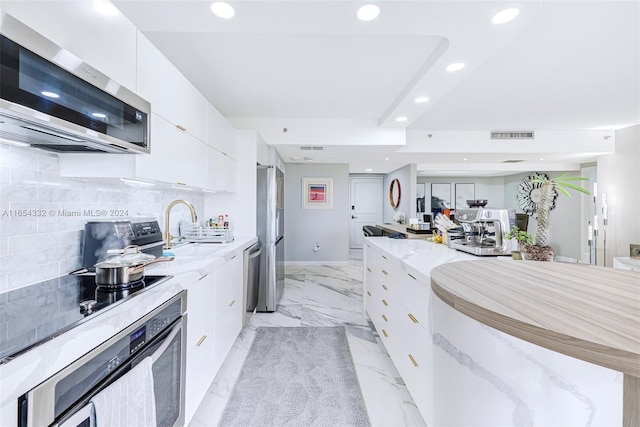 kitchen featuring light stone counters, sink, white cabinetry, decorative backsplash, and appliances with stainless steel finishes