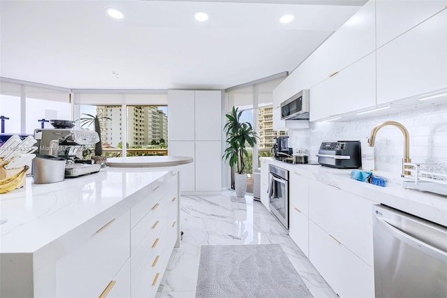 kitchen featuring light stone countertops, stainless steel appliances, tasteful backsplash, and white cabinetry