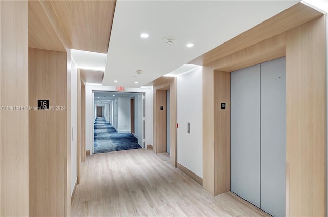 hall featuring light wood finished floors, recessed lighting, baseboards, and elevator