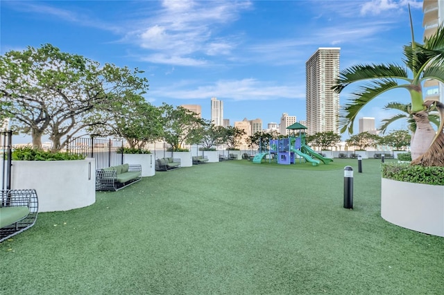 view of home's community with a city view, a lawn, playground community, and fence