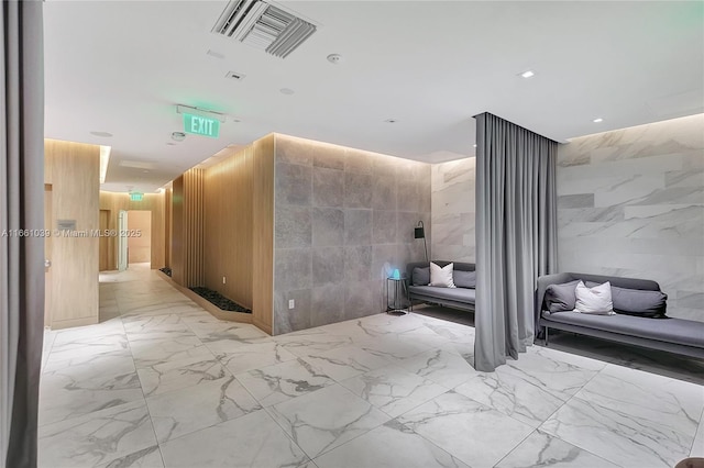 corridor featuring tile walls, stone wall, visible vents, and marble finish floor