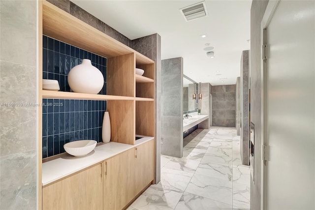 full bath featuring visible vents, a tub to relax in, marble finish floor, tile walls, and vanity