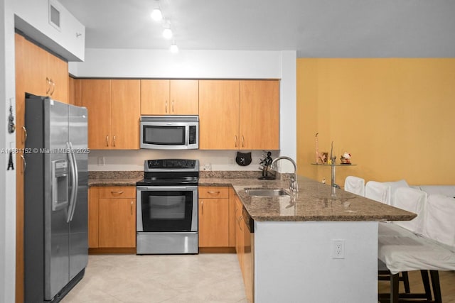 kitchen featuring dark stone counters, sink, appliances with stainless steel finishes, a kitchen bar, and kitchen peninsula