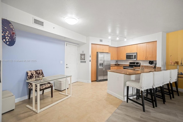 kitchen with kitchen peninsula, stainless steel appliances, dark stone counters, and a breakfast bar area