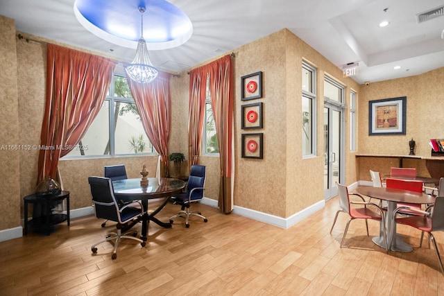 office space featuring a notable chandelier, a raised ceiling, and light hardwood / wood-style flooring