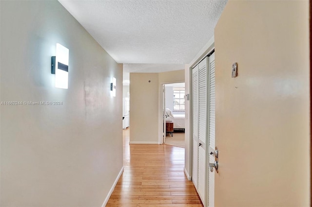 hallway with a textured ceiling and light hardwood / wood-style flooring