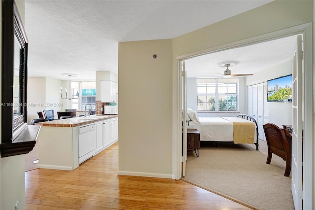 bedroom with ceiling fan with notable chandelier, light wood-type flooring, a textured ceiling, and sink