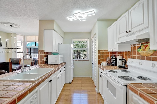 kitchen with sink, white cabinets, hanging light fixtures, white appliances, and tile countertops