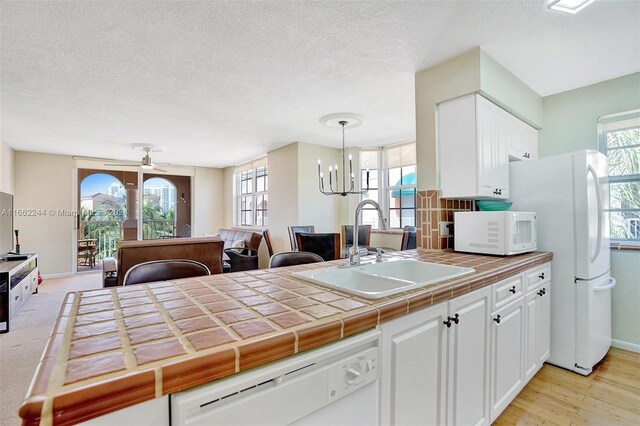 kitchen with pendant lighting, light wood-type flooring, tile counters, white cabinetry, and white appliances