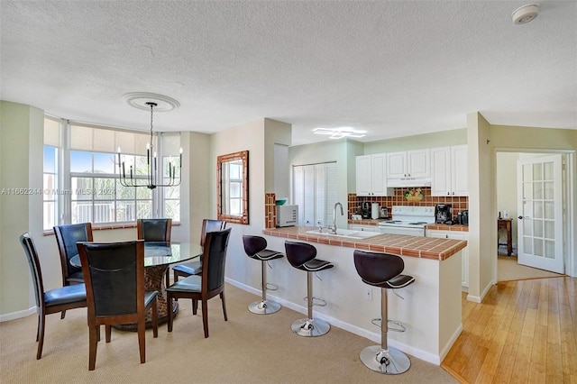 kitchen featuring light hardwood / wood-style floors, tile counters, sink, hanging light fixtures, and white range with electric stovetop