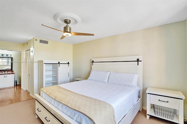 bedroom featuring light hardwood / wood-style floors, ceiling fan, and a barn door