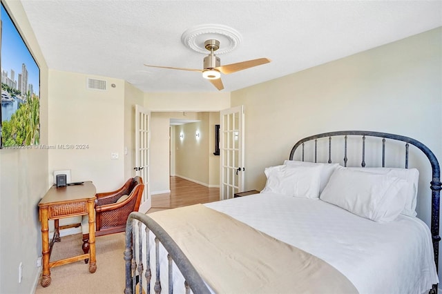 bedroom with ceiling fan, a textured ceiling, light hardwood / wood-style floors, and french doors