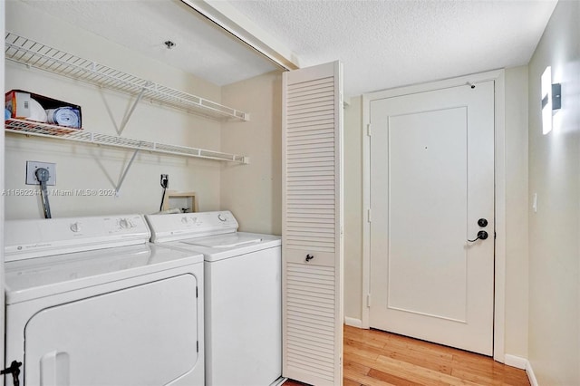 laundry area featuring a textured ceiling, light hardwood / wood-style floors, and washing machine and clothes dryer