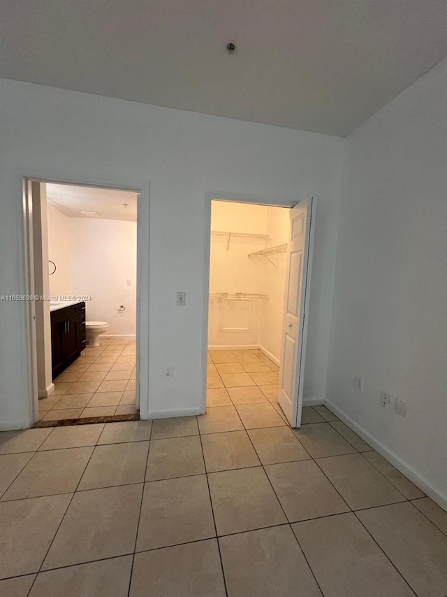 unfurnished bedroom with connected bathroom, light tile patterned floors, and a spacious closet