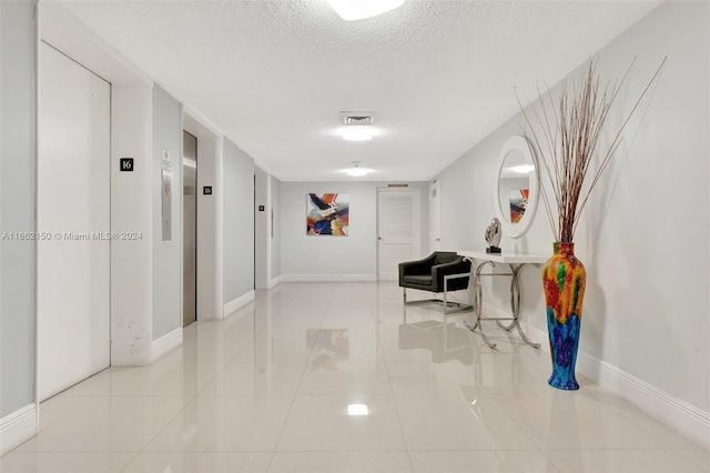 corridor featuring light tile patterned floors, a textured ceiling, and elevator