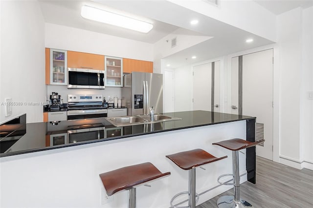 kitchen with a kitchen bar, kitchen peninsula, stainless steel appliances, sink, and light hardwood / wood-style flooring