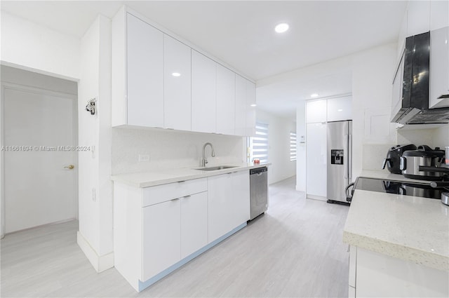 kitchen featuring light wood-type flooring, sink, white cabinets, stainless steel appliances, and backsplash