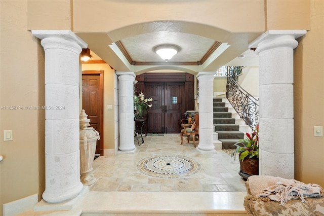 foyer entrance featuring crown molding, ornate columns, and a raised ceiling