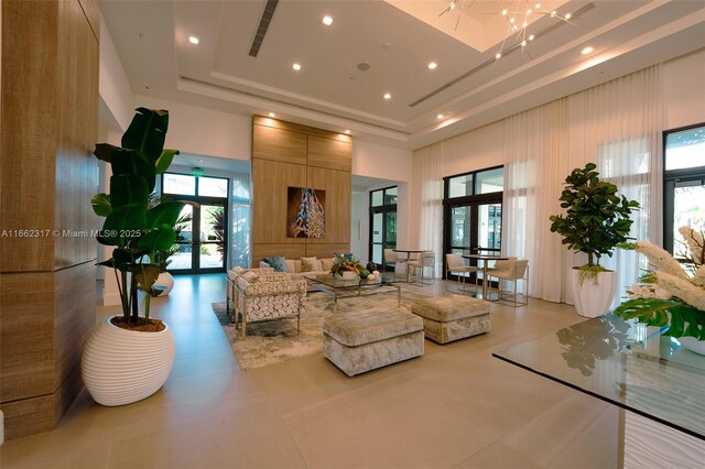 tiled living room with a tray ceiling, a towering ceiling, french doors, and a notable chandelier