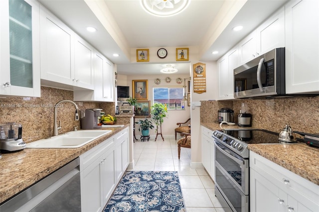 kitchen featuring light stone counters, white cabinets, light tile patterned floors, stainless steel appliances, and sink