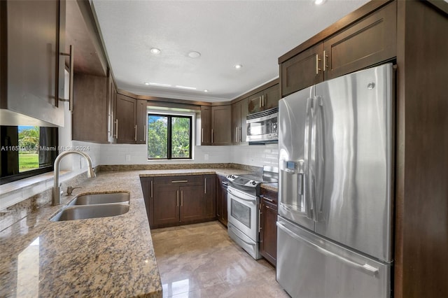 kitchen featuring dark brown cabinetry, light stone countertops, sink, stainless steel appliances, and decorative backsplash