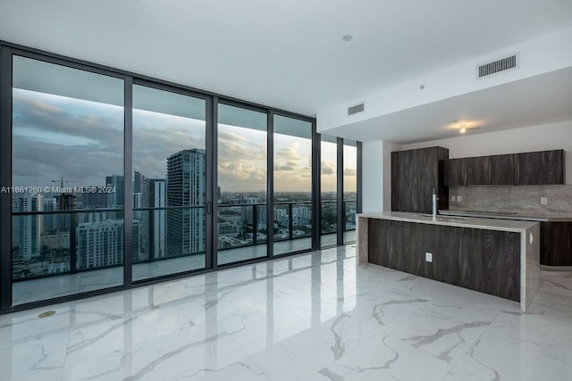 kitchen with a wall of windows, a kitchen island with sink, dark brown cabinets, and sink