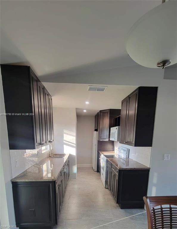 kitchen with dark brown cabinets, sink, decorative backsplash, white appliances, and light stone countertops