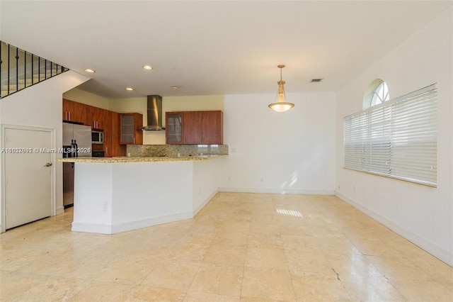 kitchen with pendant lighting, kitchen peninsula, wall chimney exhaust hood, backsplash, and appliances with stainless steel finishes