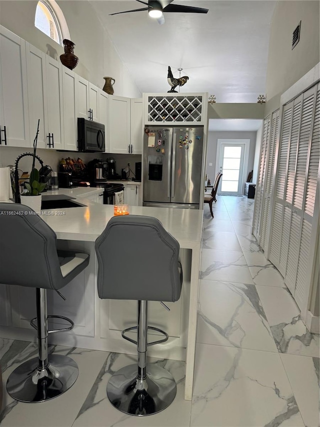 kitchen featuring appliances with stainless steel finishes, white cabinetry, a breakfast bar area, and ceiling fan