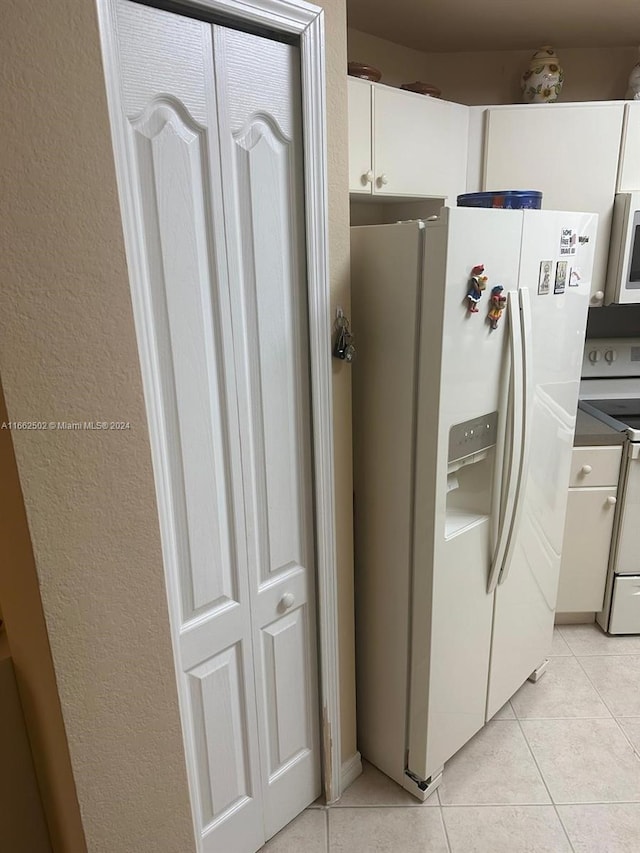 kitchen with light tile patterned flooring, white fridge with ice dispenser, electric stove, and white cabinets