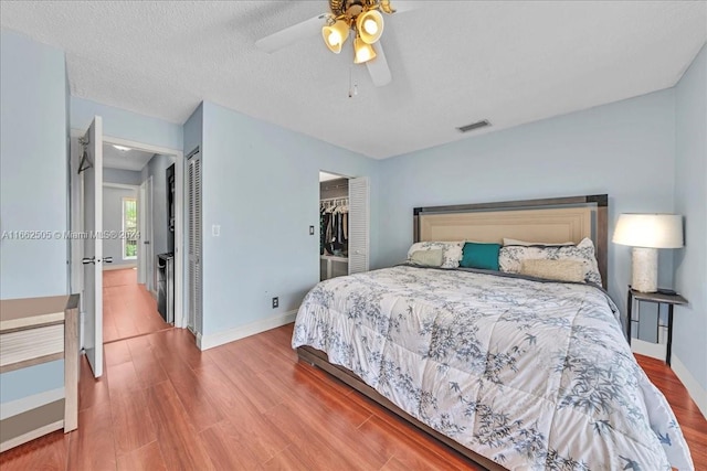 bedroom featuring a spacious closet, a textured ceiling, hardwood / wood-style floors, a closet, and ceiling fan