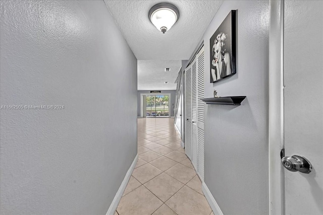 corridor featuring a textured ceiling and light tile patterned floors